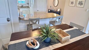 A dining area with a dark wooden table, chairs, a potted plant, and a woven basket. - Driftwood Towers (Gulf Shores)