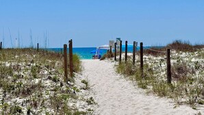 A sandy beach path leading to a beach area with a blue umbrella and a sign. - Driftwood Towers (Gulf Shores)
