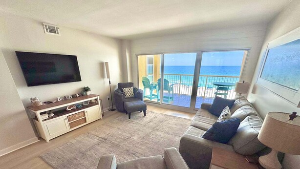 A living room with a TV, sofa, armchair, and a balcony with a view of the sea. - Driftwood Towers (Gulf Shores)
