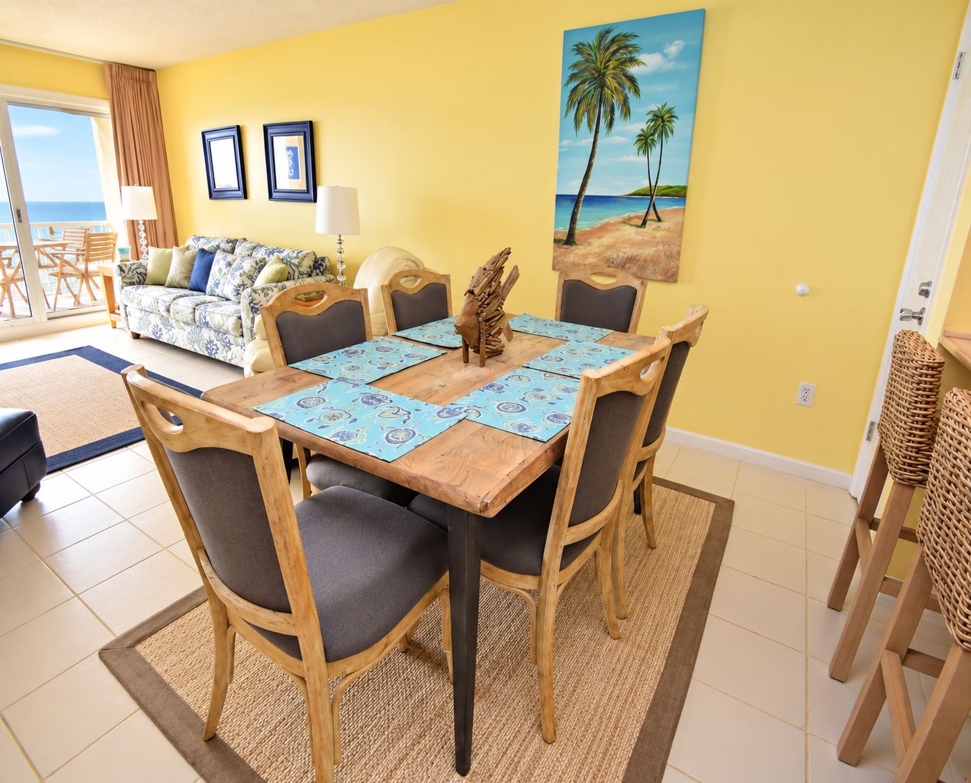 A dining area with a wooden table, chairs, and a beach-themed painting on the wall.