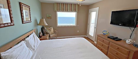 A hotel room with a bed, a ceiling fan, a television, and a window with a view of the ocean.