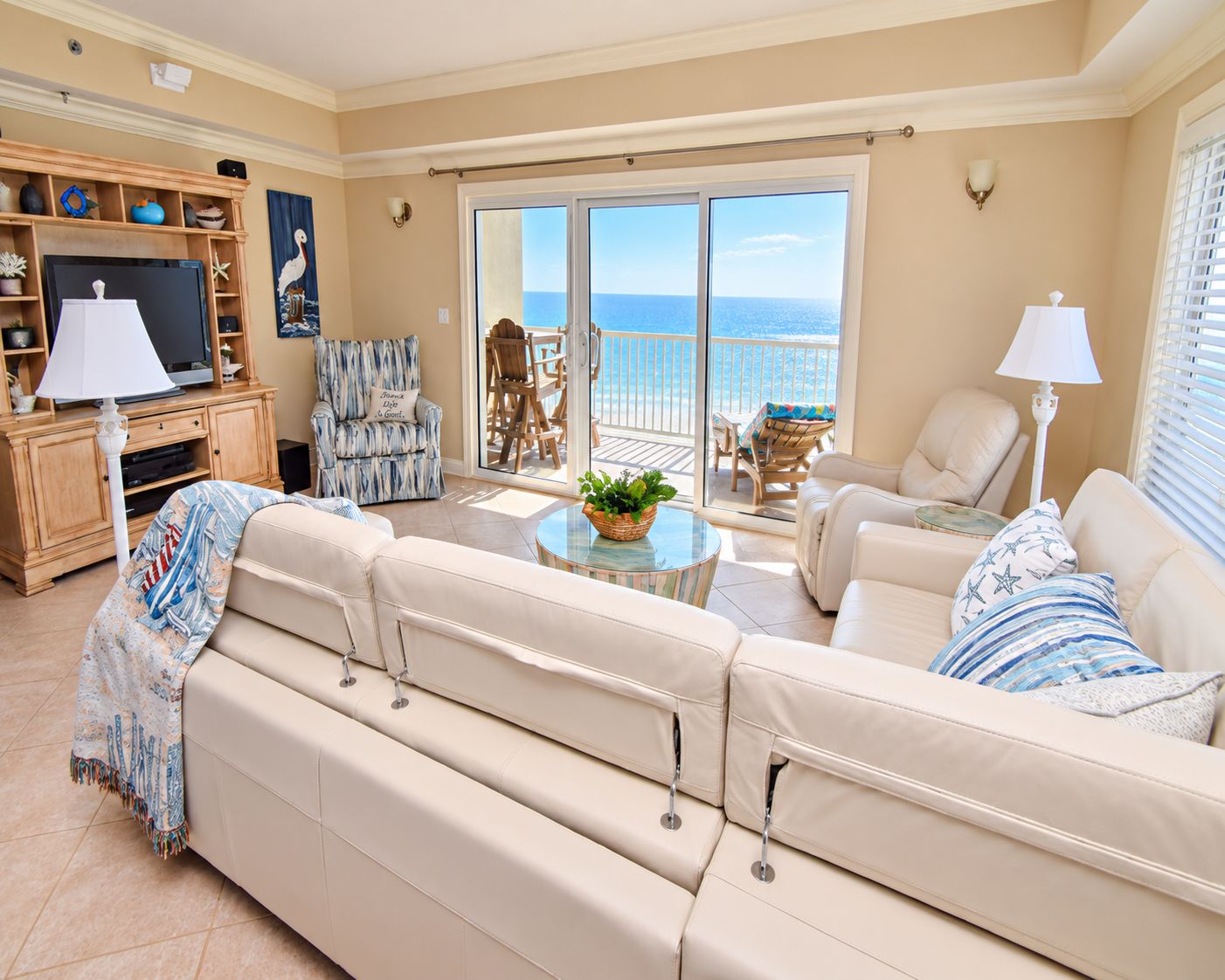A spacious living area with a large sofa, a television, and a balcony with a view of the ocean.