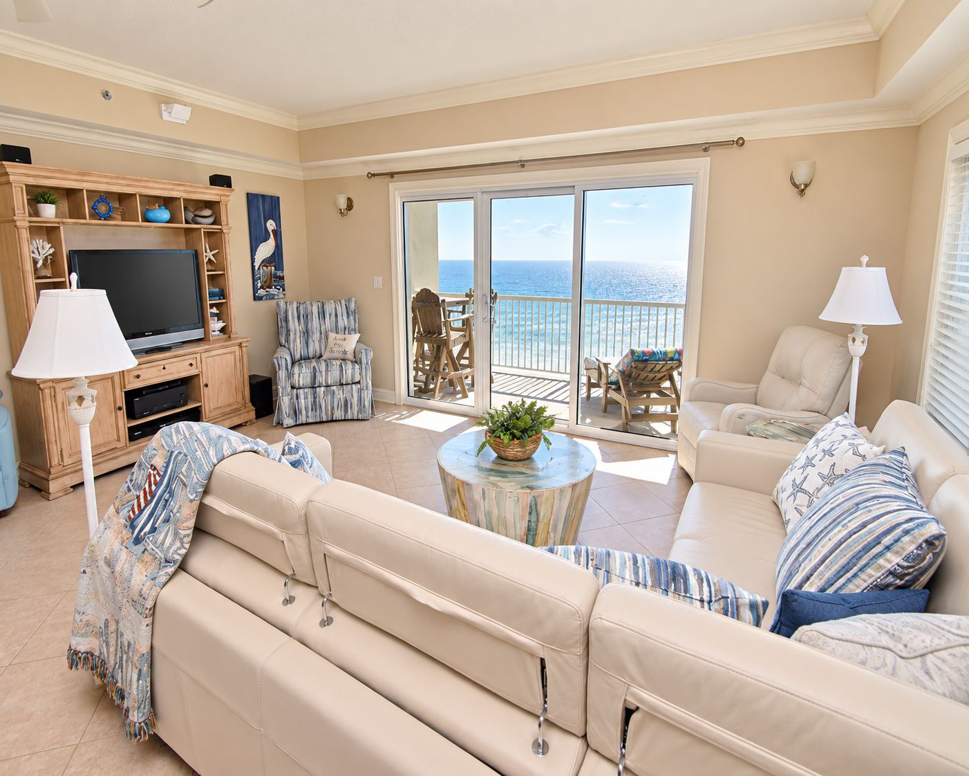Un salón amplio con una televisión grande, asientos cómodos, un balcón con vista al mar y una estantería decorativa.