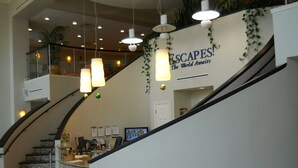 A hotel lobby with a staircase, a reception desk, and a sign that reads "ESCAPES! The World Awaits".