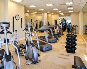 Un gimnasio con diversas máquinas de cardio, equipo de levantamiento de pesas y un reloj en la pared.