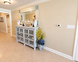 A hallway with a white console table, a mirror, and a thermostat on the wall. - Escapes To The Shores (Orange Beach)