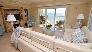 A living room with a sofa, TV, and a view of the ocean through a sliding door.
