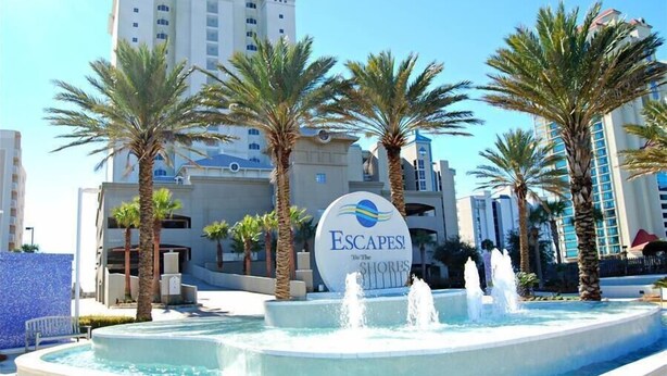 A hotel sign with the name 'Escapes! The Shores' and a water feature with palm trees.