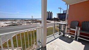 Un balcón con vistas a la playa y a una carretera, con dos sillas Adirondack y una pequeña mesa.