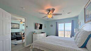 Un dormitorio con cama, ventilador de techo, televisor y vistas al exterior.