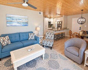 A living room with a blue sofa, patterned armchairs, a white coffee table, and a patterned rug. - Gulf House (Gulf Shores)