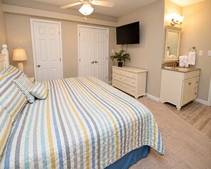 A bedroom with a bed, a dresser, a television, and a bathroom vanity. - Gulf House (Gulf Shores)