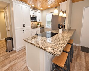 A kitchen with white cabinets, a granite countertop, stainless steel appliances, and wooden stools. - Gulf House (Gulf Shores)