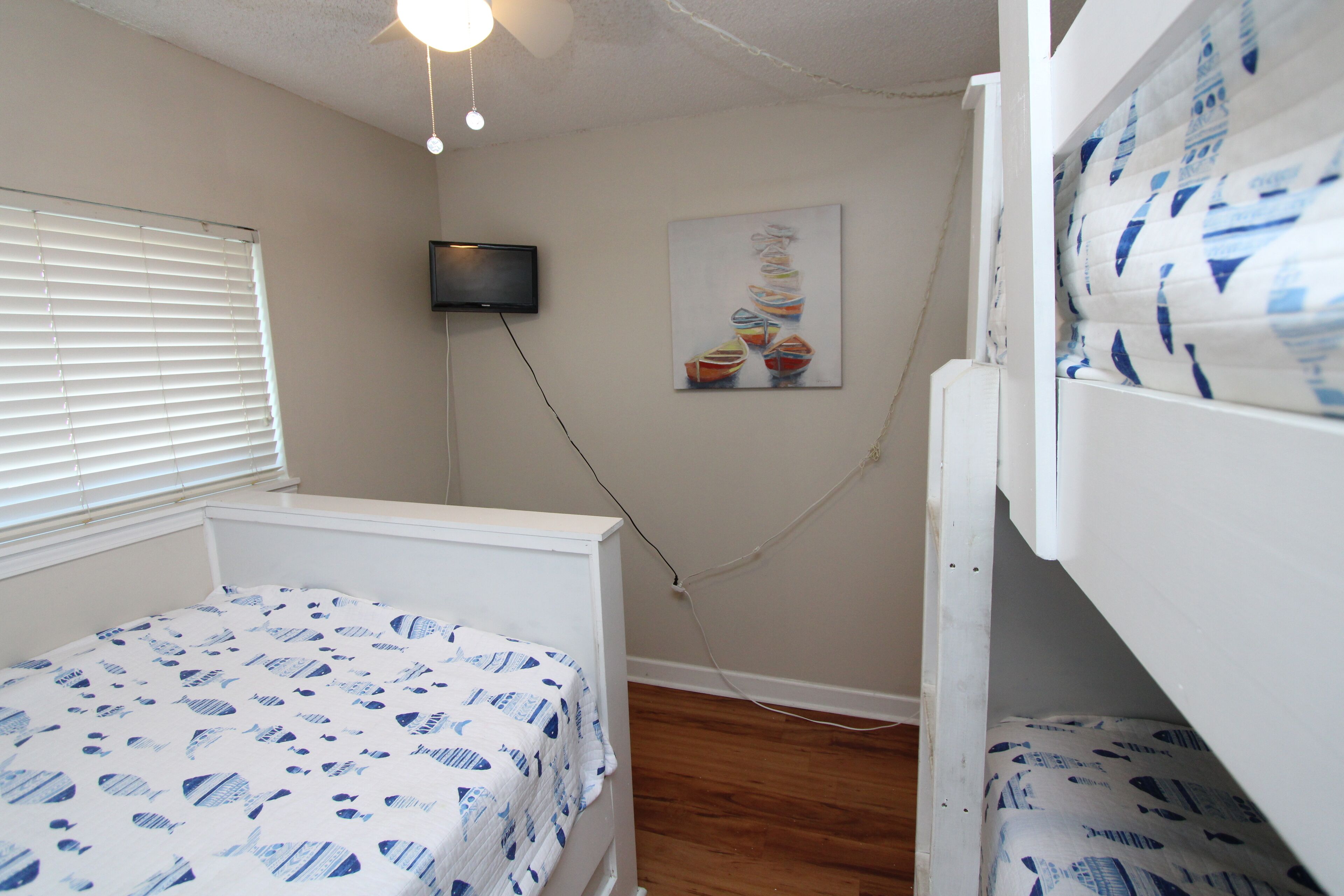 A bedroom with a bunk bed, a television mounted on the wall, and a window with blinds.