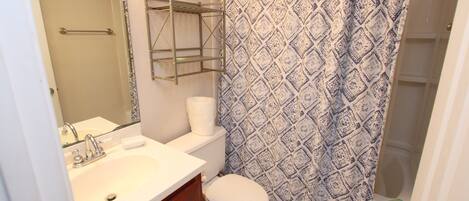 Een badkamer met een wit wastafelmeubel, toilet en douchegordijn.