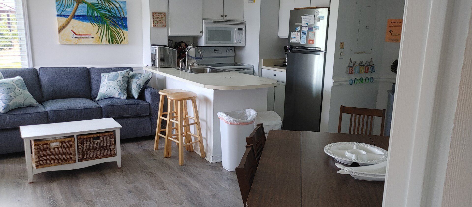A compact living space with a kitchenette, a sofa, a dining table, and a trash bin.