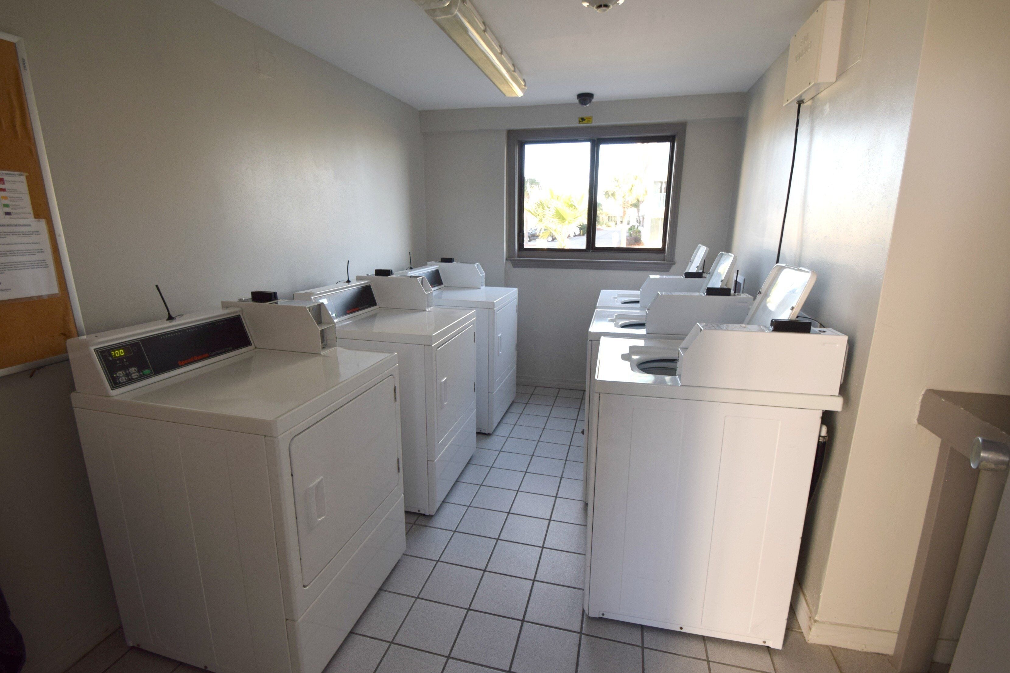 A laundry room with four washing machines, a dryer, and a window providing natural light.