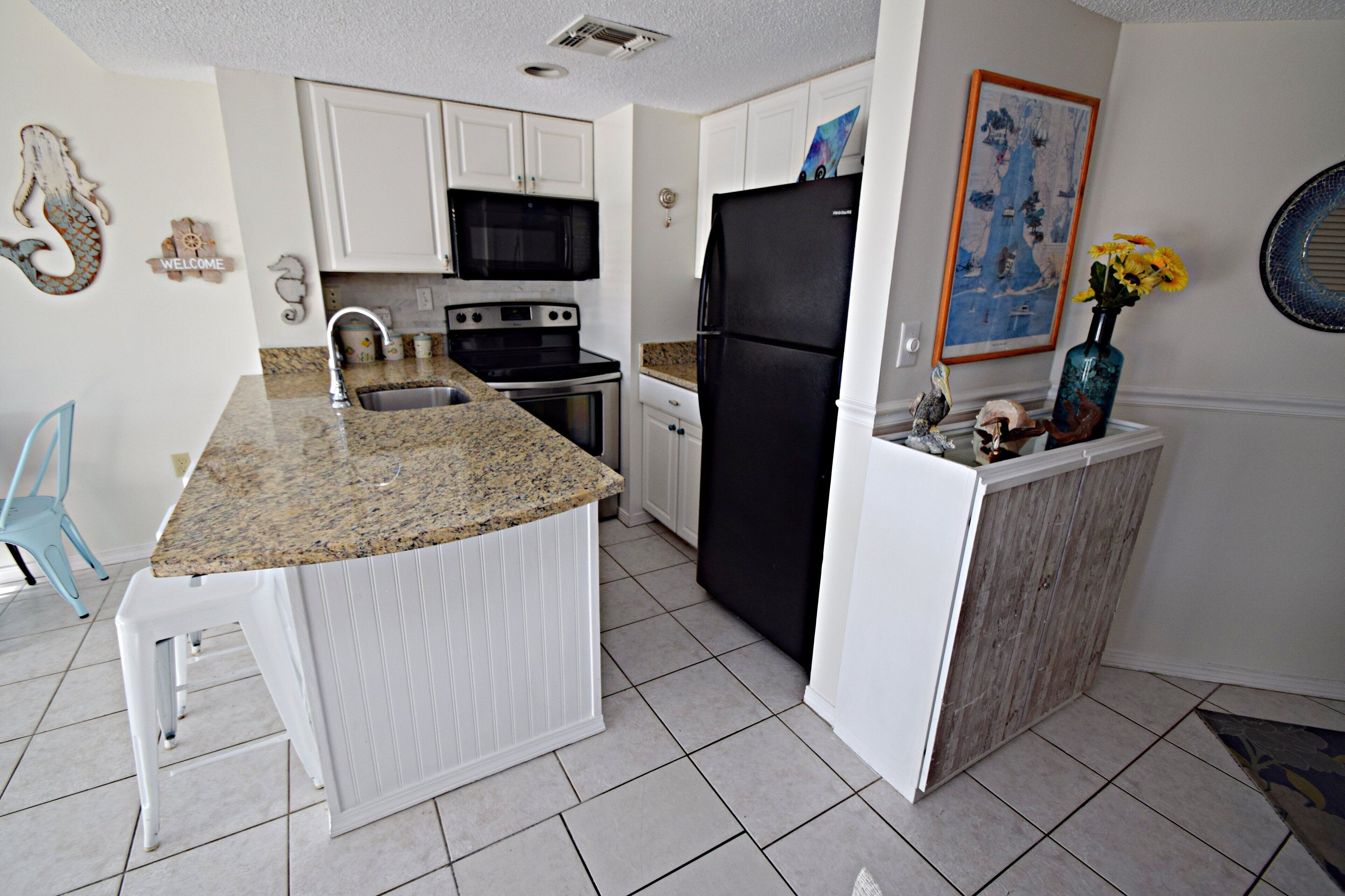 A compact kitchen with white cabinets, a black refrigerator, a microwave, and a granite countertop.