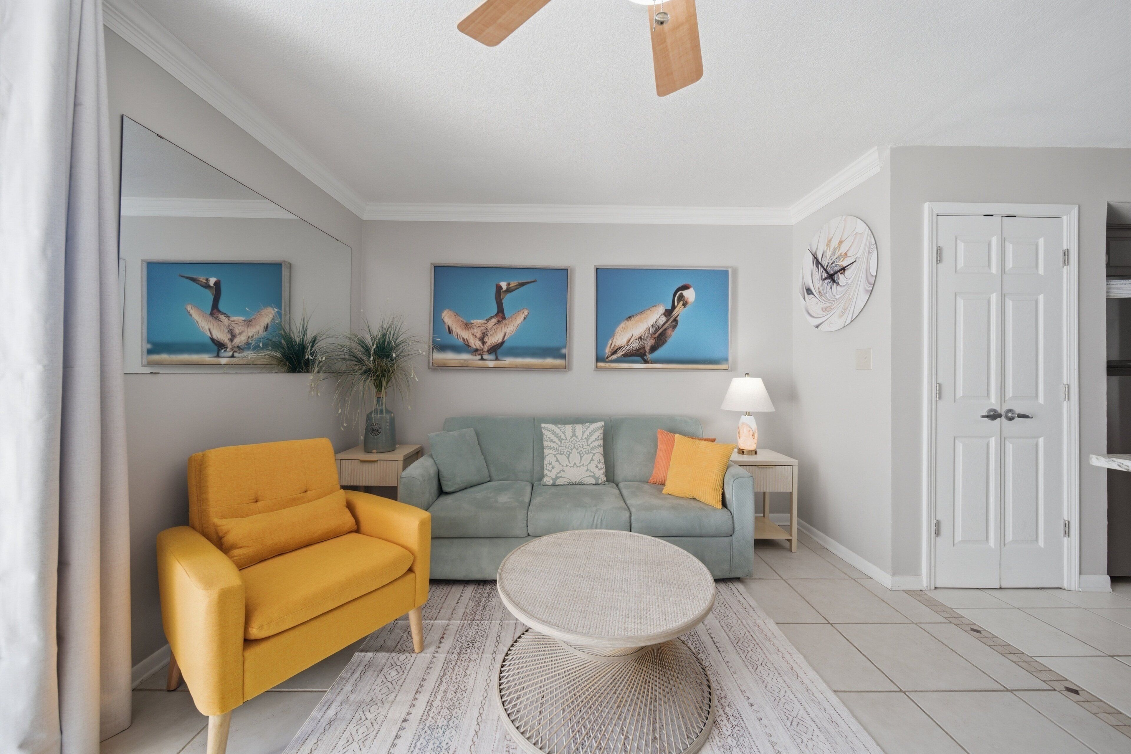 A living room with a sofa, armchair, round table, and wall art.