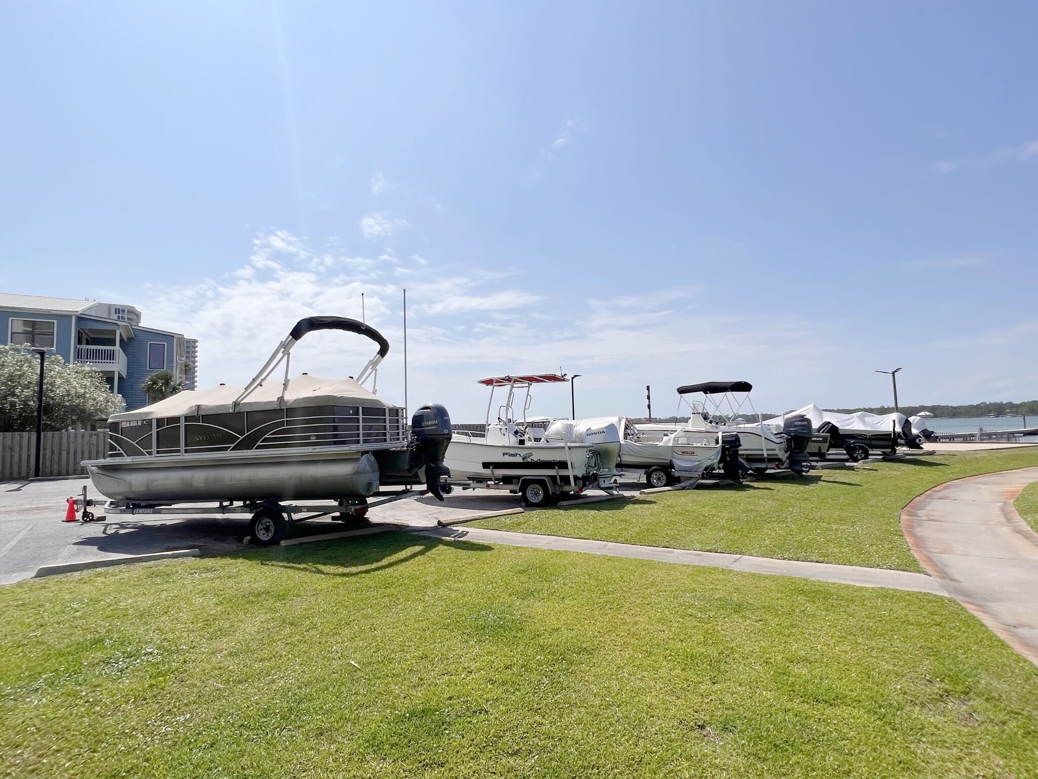 A row of boats parked on a grassy area near a body of water, with a building in the background.