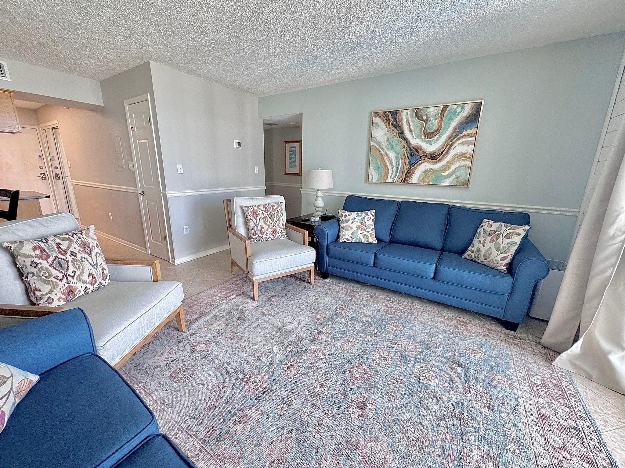 A living room with a blue sofa, a white armchair, and a patterned rug.