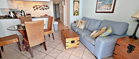 A living room with a sofa, chairs, a coffee table, a dining area with a table and chairs, a kitchen area, and a sign that reads "SAILING".