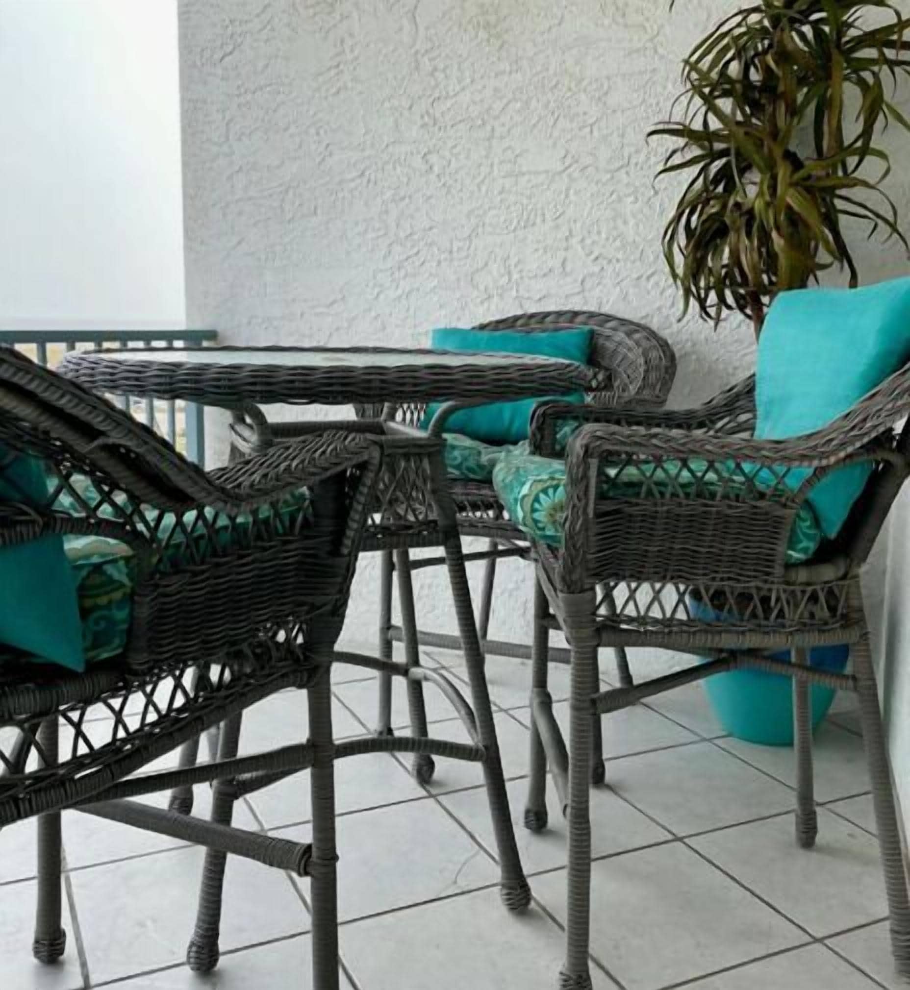 Wicker furniture with teal cushions, a potted plant, and a white textured wall.