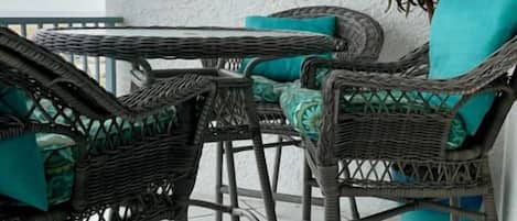 Mueble de mimbre con cojines azul turquesa, una planta en maceta y una pared blanca con textura.