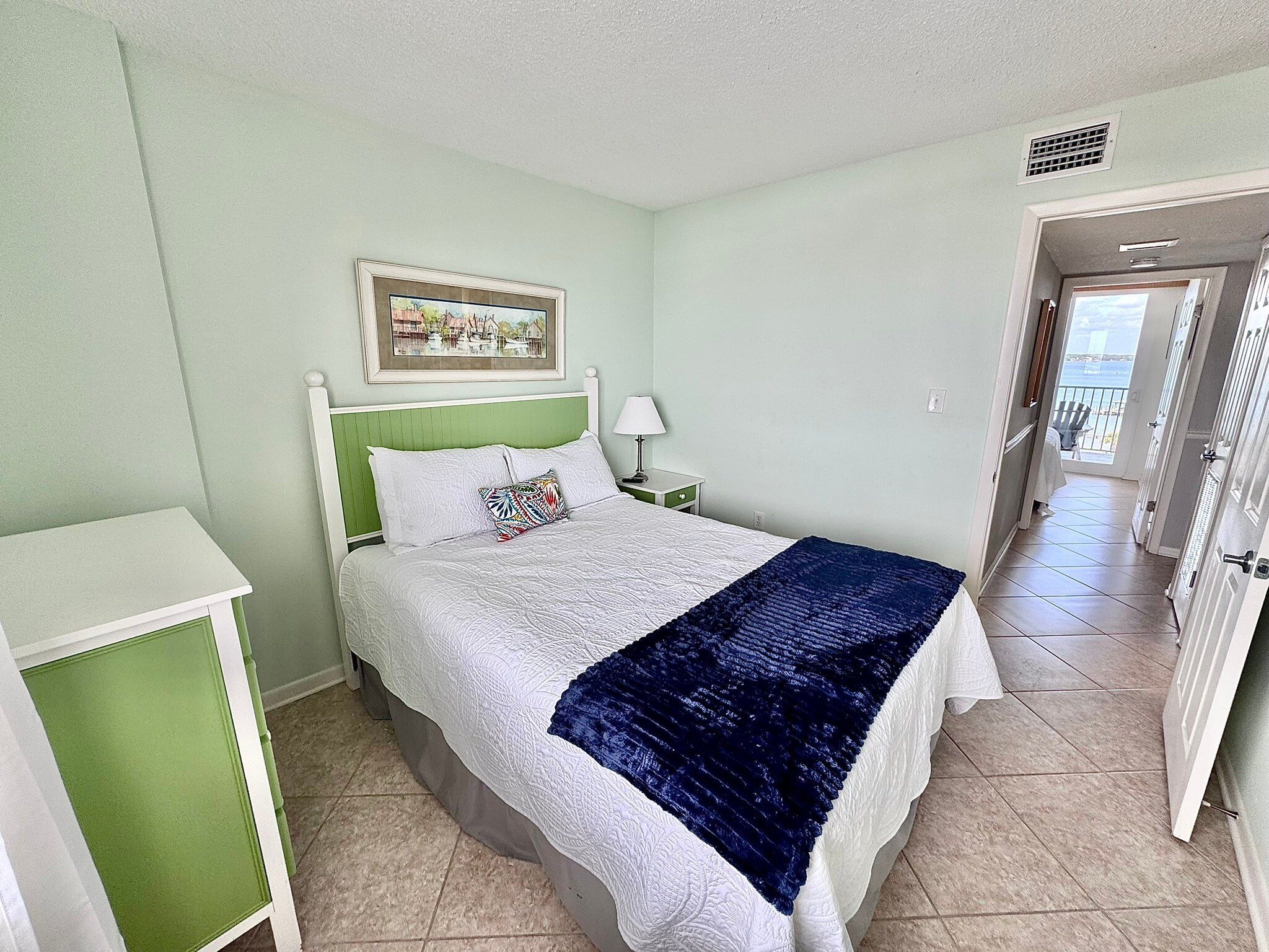 A bedroom with a bed, a nightstand, a green cabinet, and a door leading to a balcony.