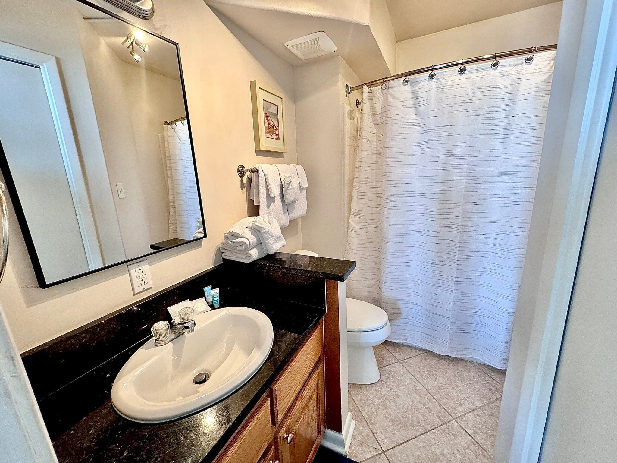 A bathroom with a white sink, a mirror, a toilet, and a shower curtain.