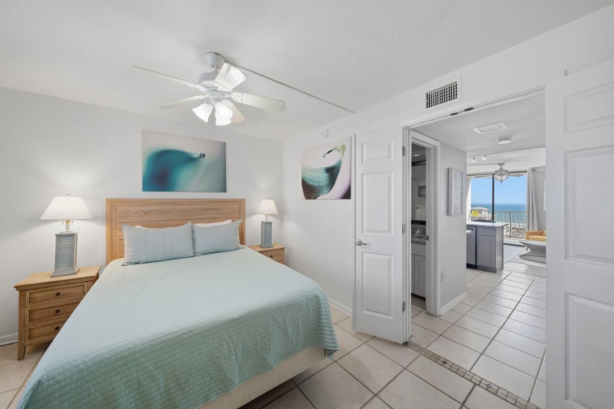 A bedroom with a bed, nightstands, a ceiling fan, and artwork on the walls.