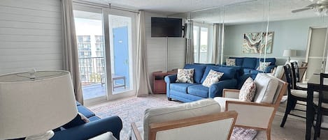 Uma sala de estar com um sofá azul, uma mesa de centro de madeira e uma TV fixada na parede.