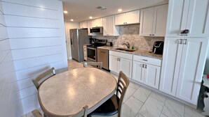 A modern kitchen with white cabinetry, a central island, and a dining area with a round table and chairs. - Gulf Shores Surf & Racquet Club (Gulf Shores)
