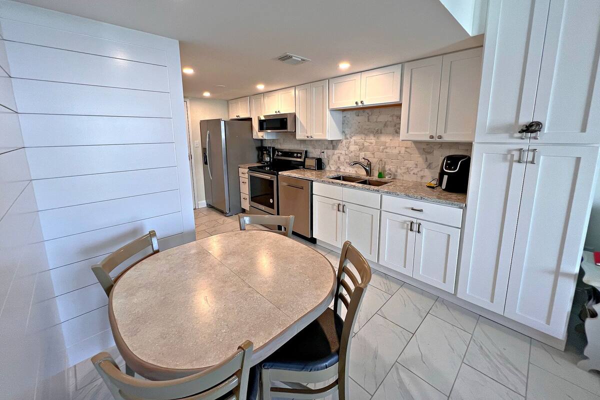 A modern kitchen with white cabinetry, a central island, and a dining area with a round table and chairs.