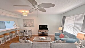 Un salon équipé d’un ventilateur de plafond, d’un téléviseur, d’un canapé, d’une table basse et d’un coin repas avec des chaises et une table.