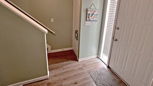 Un couloir avec un plancher en bois, une porte portant l’inscription « MAISON DE PLAGE » et un petit élément décoratif mural.
