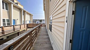Une terrasse en bois mène à un bâtiment dont le revêtement extérieur est de couleur beige et la porte est bleue.