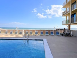 A pool area with a view of the ocean, a wooden deck, and a building with balconies.