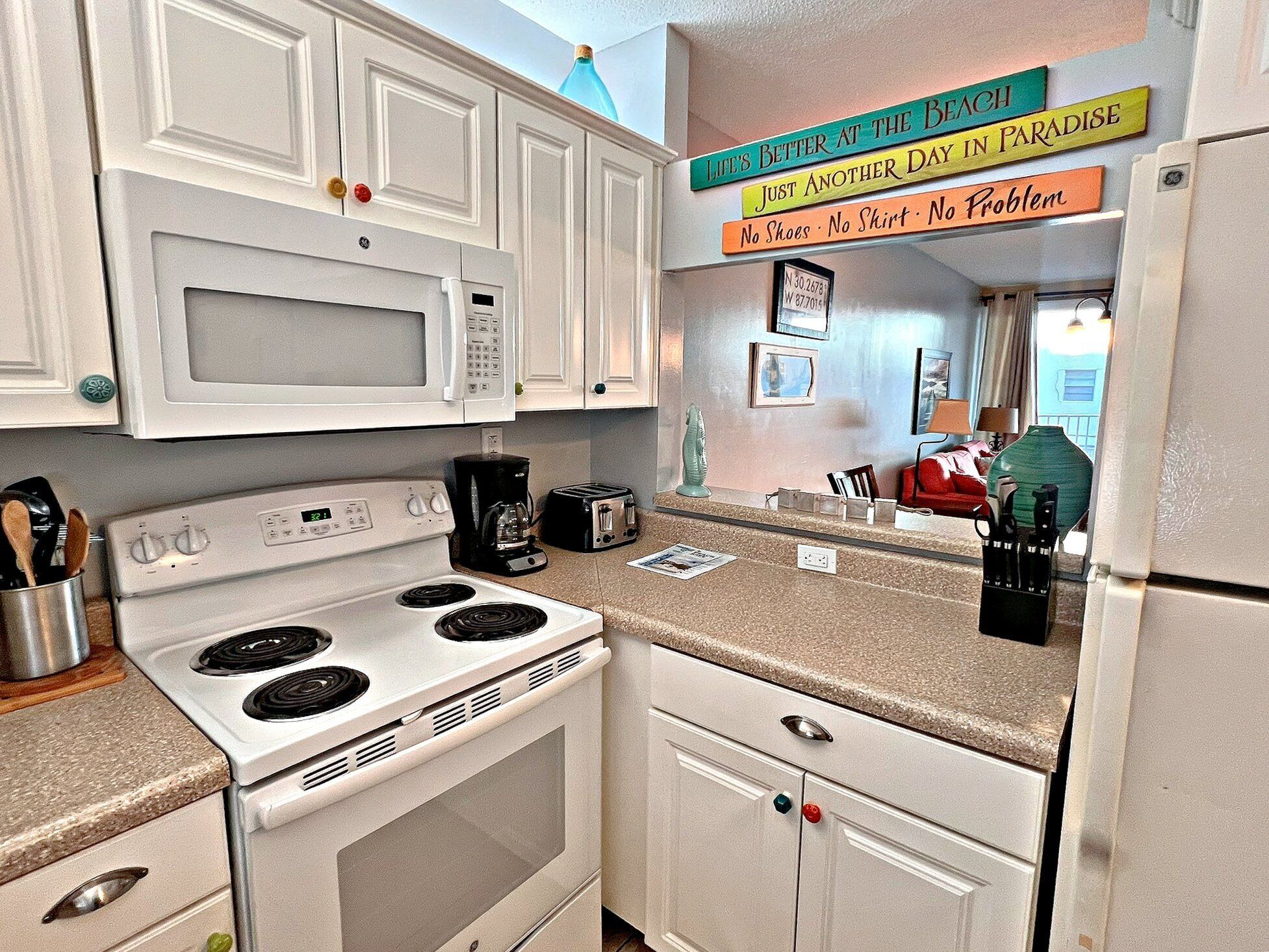 A kitchen with white cabinets, a microwave, stove, and a refrigerator. There are signs on the wall with motivational phrases.