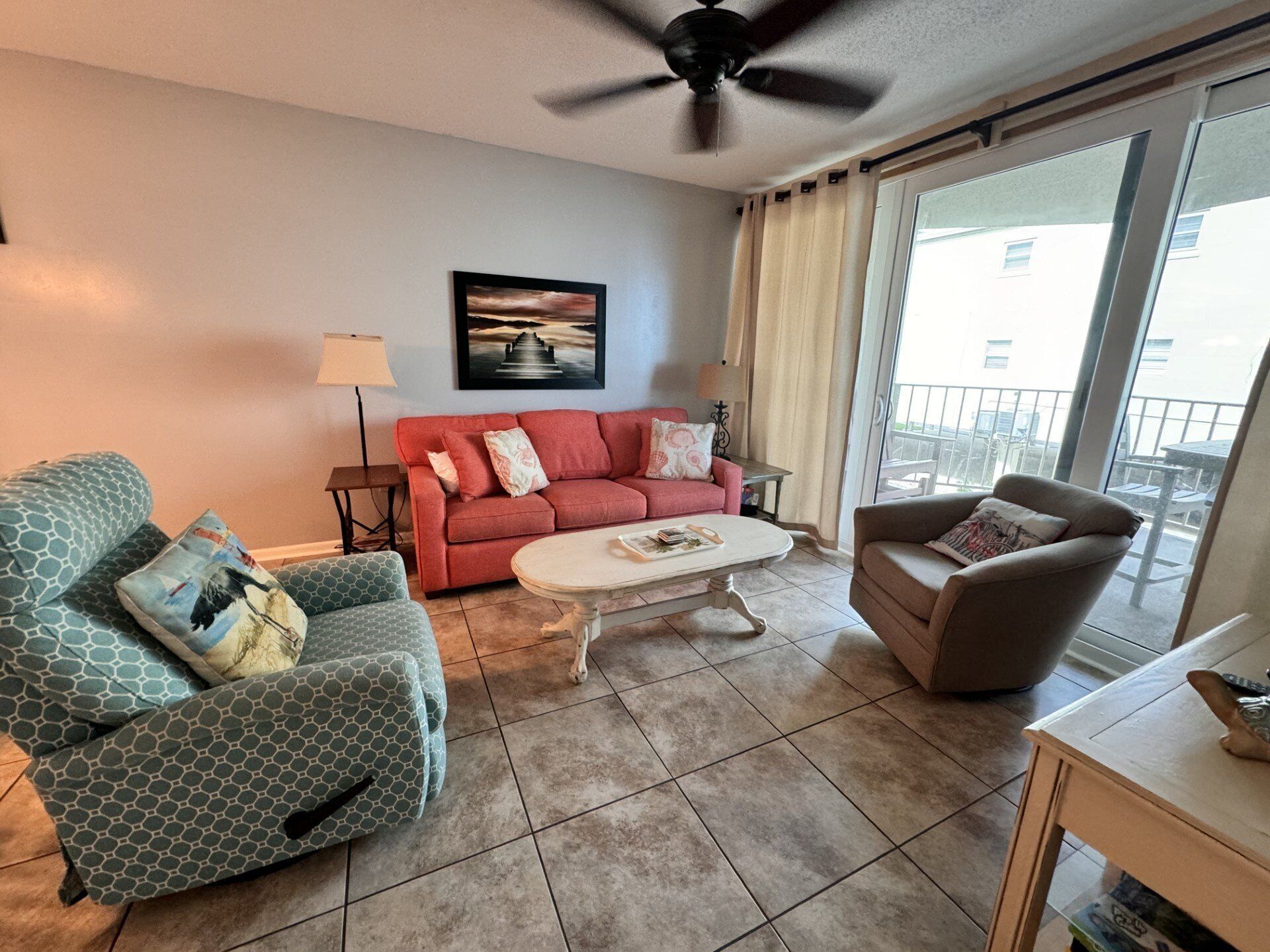 A living room with a red sofa, a green patterned armchair, a brown armchair, a white coffee table, and a ceiling fan.
