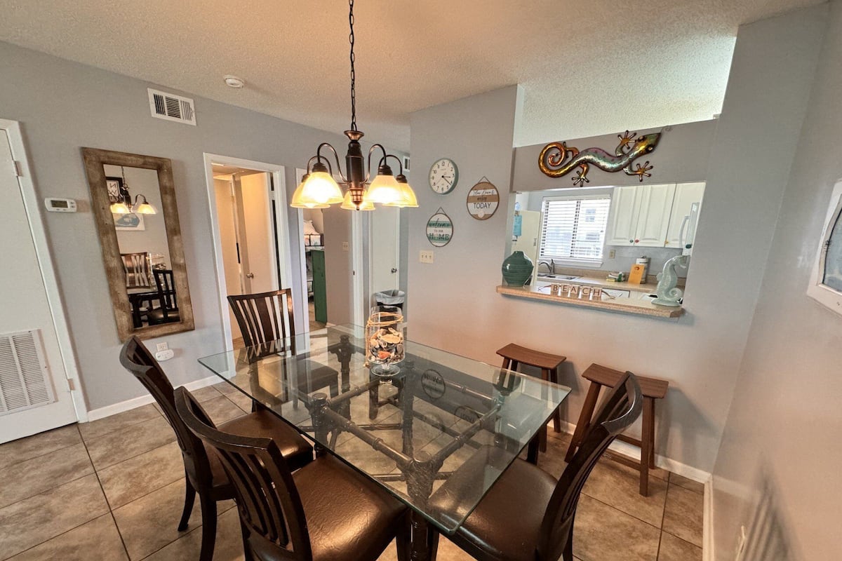 A dining area with a glass-top table, dark wooden chairs, and a pendant light fixture.
