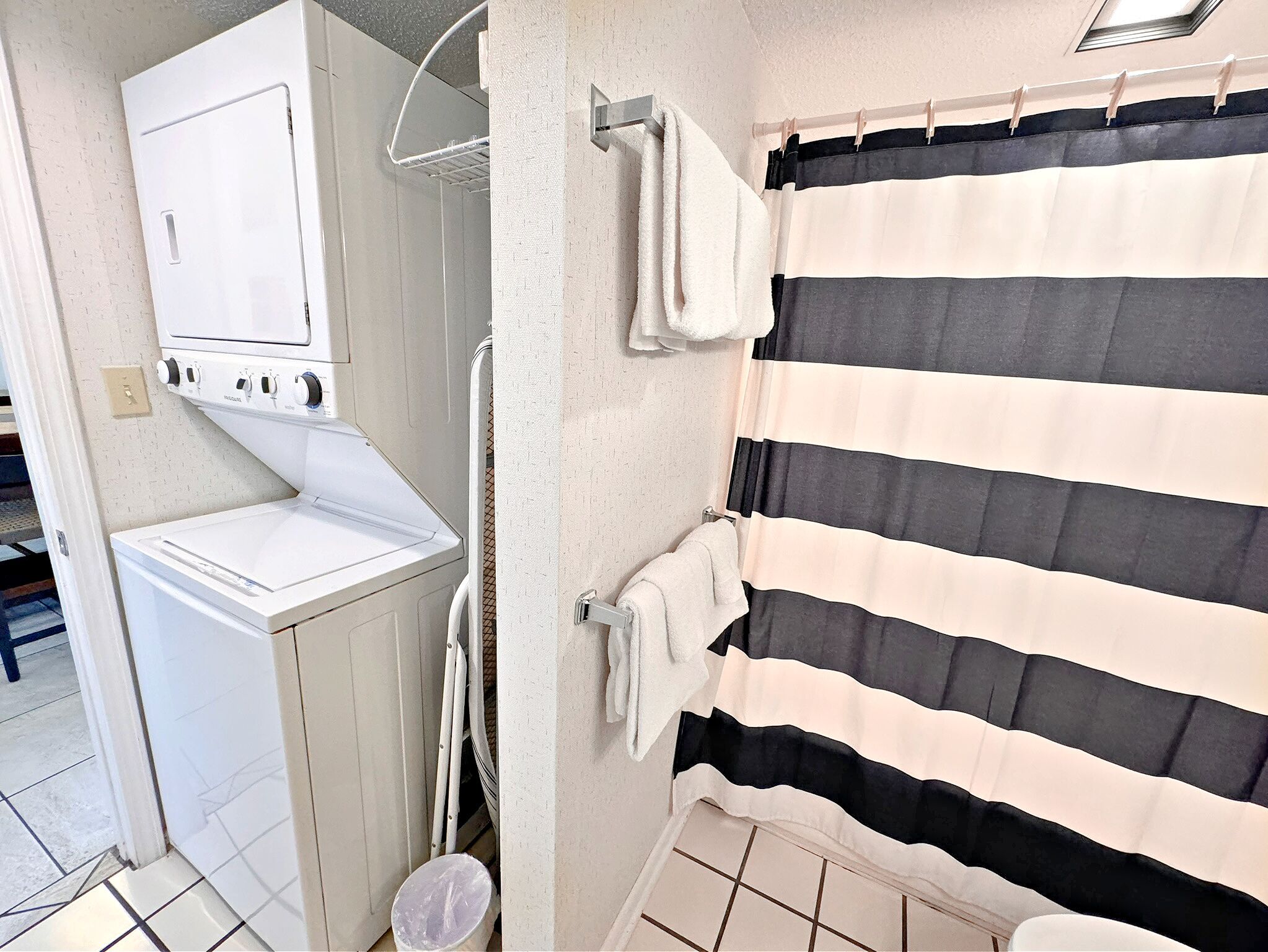 A laundry area with a washing machine, a drying rack, and a striped shower curtain.
