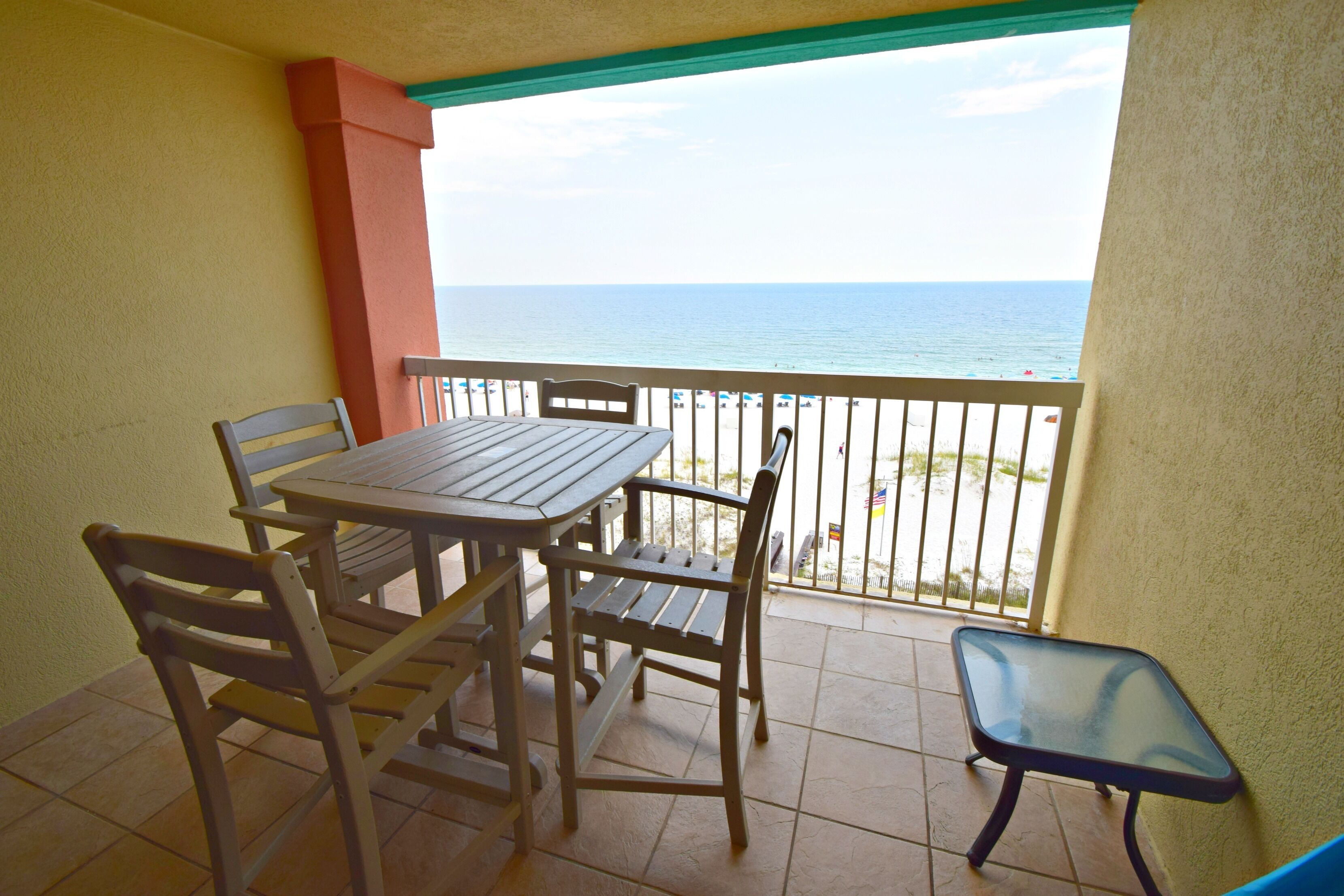 A balcony with a table and chairs, a small table, and a view of the ocean.