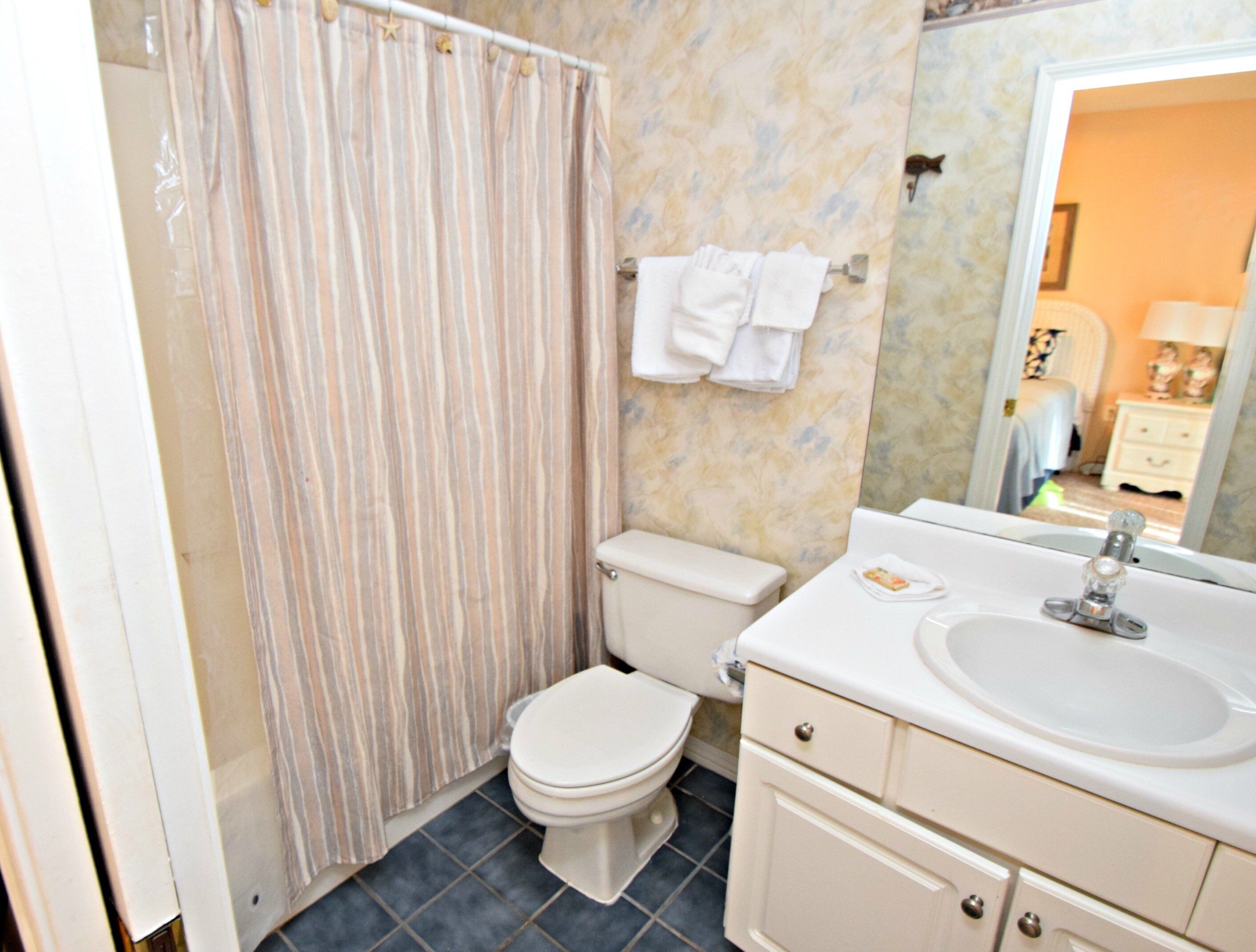 Une salle de bain avec un rideau de douche à rayures, des toilettes, un lavabo avec un miroir et un porte-serviettes avec des serviettes.