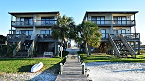Un hotel fronte spiaggia con una passerella in legno che conduce all'ingresso, palme e una postazione di salvataggio.
