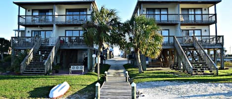 Un hotel frente a la playa con un paseo marítimo de madera que conduce a la entrada, palmeras y un puesto de salvavidas.