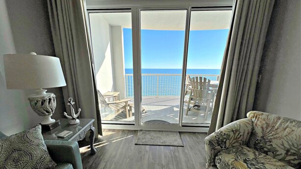 Una camera d'albergo con balcone, un divano, una sedia, una lampada e vista sull'oceano.