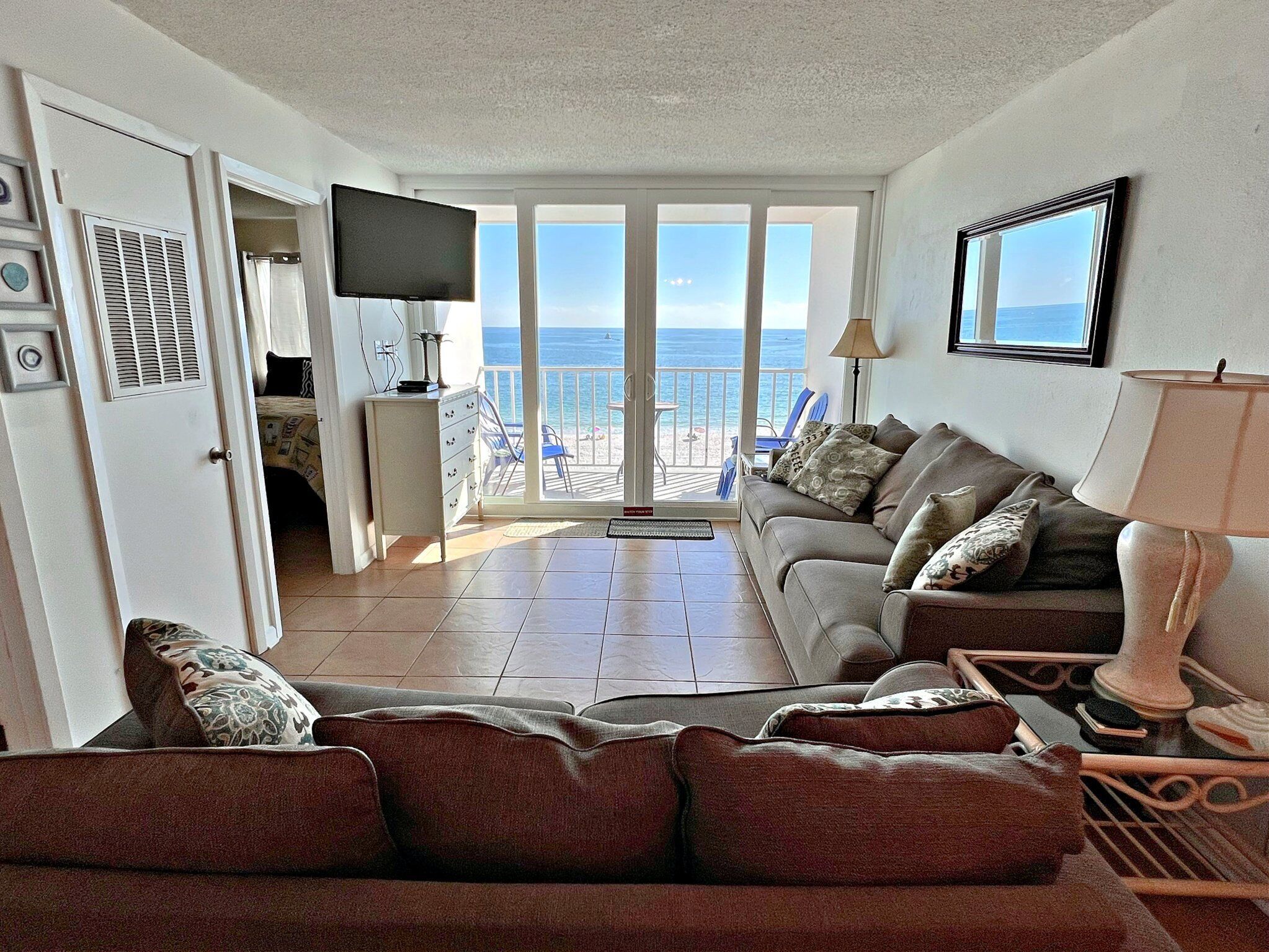 Een woonkamer met een bank, een televisie en uitzicht op de zee door grote ramen.