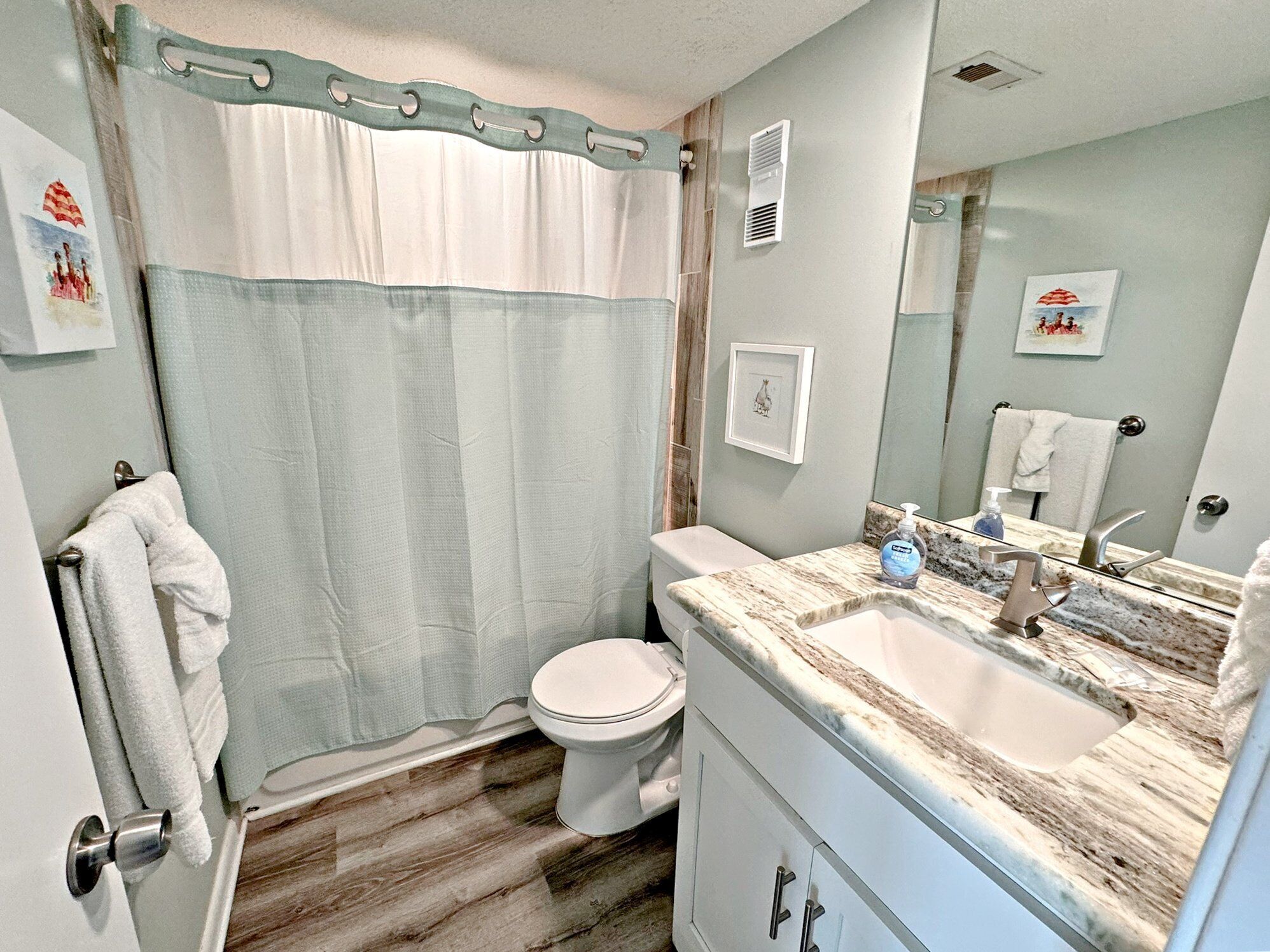 Un baño con cortina de ducha, inodoro, lavabo con encimera de mármol y espejo.