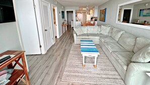 Ein modernes Wohnzimmer mit einem Ecksofa, einem Couchtisch aus Holz und einer Küche im Hintergrund.
